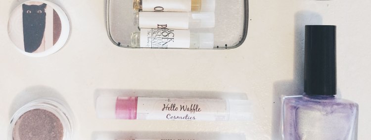 various indie cosmetics in flatlay composition: eyeshadow, lipsticks, nail polish, perfume